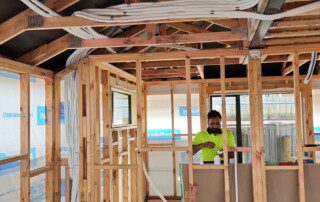 A man working on a house under construction, with a high wall and pre-pipe installation.