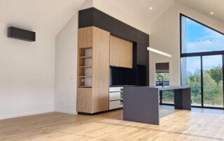 A modern kitchen with a large window, showcasing a sleek design and ample natural light. Air condition on the wall.